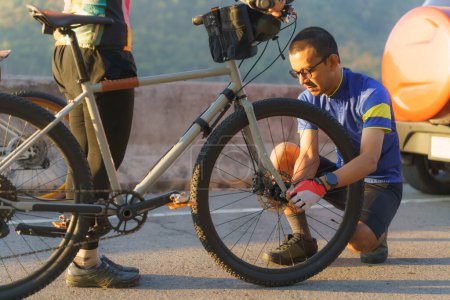 Téléchargez les photos : Asian cyclist couple assembles bikes for a morning bike ride by the lake. - en image libre de droit
