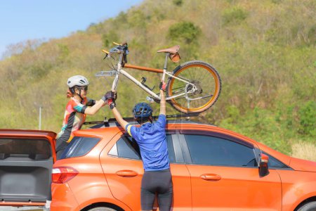 Téléchargez les photos : Asian cyclist couple unloading their bicycles from the roof of their car in preparation for a morning bike ride by the lake. - en image libre de droit