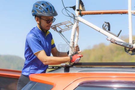 Téléchargez les photos : Asian cyclist man installing a bicycle rack on the roof of his car to store his bike after finishing his exercise bike. - en image libre de droit