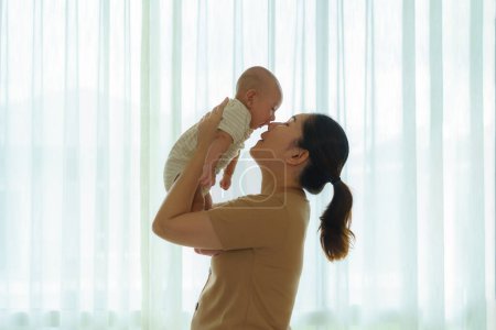 Téléchargez les photos : Mère asiatique jouant avec son nouveau-né dans la chambre à coucher à la maison. promouvoir les relations familiales et le bon développement du bébé - en image libre de droit