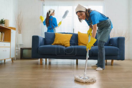 Two diligent Asian maids collaborate seamlessly, cleaning the living room with precision and efficiency, leaving no corner untouched in their pursuit of spotless perfection