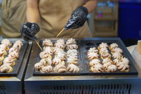 A street vendor in action, preparing Takoyaki, a popular Japanese snack made of grilled octopus balls, garnished with seasoning