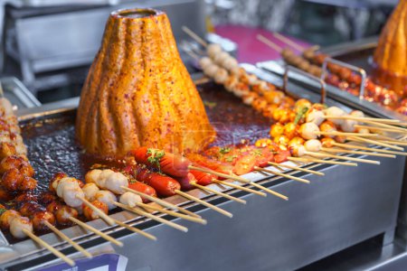 Skewered Pork Ball including sausage being cooked on a hot grill, basted with a spicy sauce, at a street food market.