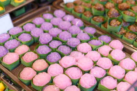 Steamed layer cake desserts crafted into flower shapes, presented in banana leaf cups, displaying an array of pink and purple colors
