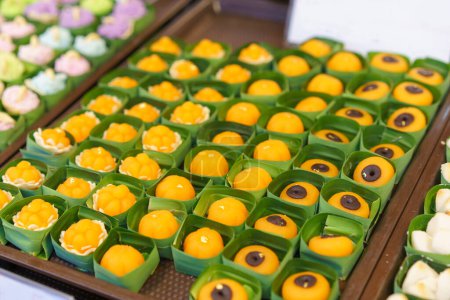 Array of colorful Thai desserts, including Thong Ek and Khanom Ja Mong Got, presented in eco-friendly banana leaf cups at a street market