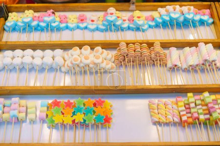 Téléchargez les photos : Une délicieuse sélection de brochettes de bonbons colorés, y compris des guimauves et des bonbons à la gelée, exposées dans un étal de marché à vendre - en image libre de droit