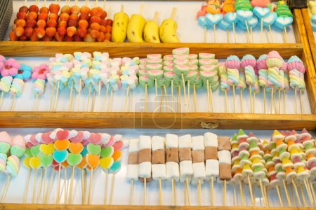 Téléchargez les photos : Une délicieuse sélection de brochettes de bonbons colorés, y compris des guimauves et des bonbons à la gelée, exposées dans un étal de marché à vendre - en image libre de droit