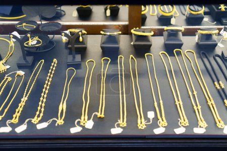 Experience the allure of opulence up close with a detailed view of gold necklaces, rings, and chains elegantly showcased in a beauty retail store window. Each piece exudes timeless sophistication, captivating passersby with its radiant charm and luxu