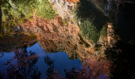 Foto de Reflejos. Rocas y vegetación de una colina reflejada en el agua de un lago - Imagen libre de derechos