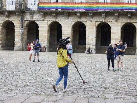 Photo for Santiago de Compostela, June 30, 2023. Camera operator. A woman with a video camera and a tripod walks through the Plaza del Obradoiro - Royalty Free Image