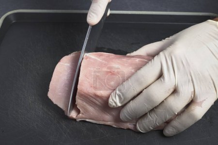 Foto de Lomo de cerdo. Las manos del hombre cortando rebanadas de carne con un cuchillo - Imagen libre de derechos