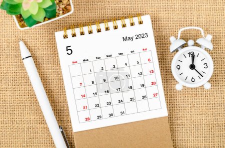 May 2023 Monthly desk calendar for the organizer to plan 2023 year with alarm clock and pen on sack background.