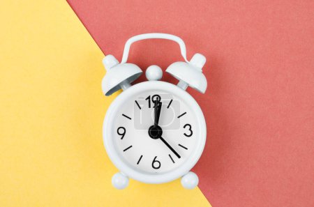 Foto de Reloj despertador vintage blanco sobre fondo rojo brillante y amarillo. - Imagen libre de derechos