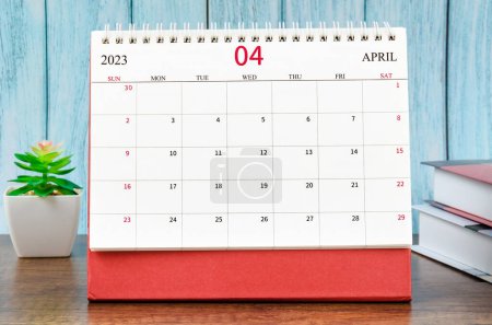 April 2023 Monthly desk calendar for 2023 year with the books on blue wooden background.