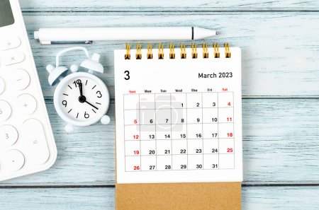 März 2023 Monatlicher Tischkalender für den Veranstalter zur Planung des Jahres 2023 mit Wecker und Taschenrechner auf Holztisch.