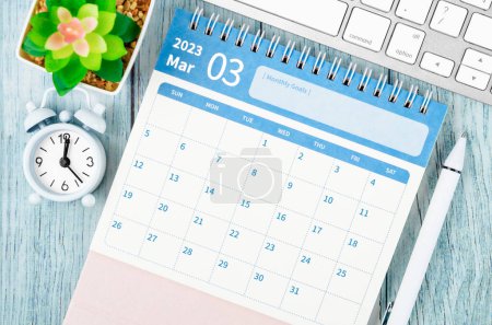 März 2023 Monatlicher Tischkalender für den Veranstalter zur Planung des Jahres 2023 mit Wecker auf Holztisch.