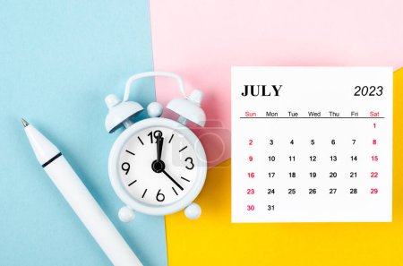 Foto de July 2023 Monthly calendar with alarm clock and pen on beautiful background. - Imagen libre de derechos