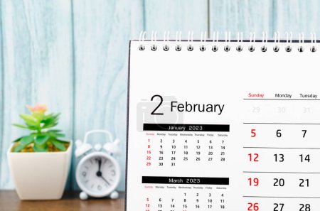 Foto de February 2023 Monthly desk calendar for 2023 year with alarm clock on blue wooden background. - Imagen libre de derechos