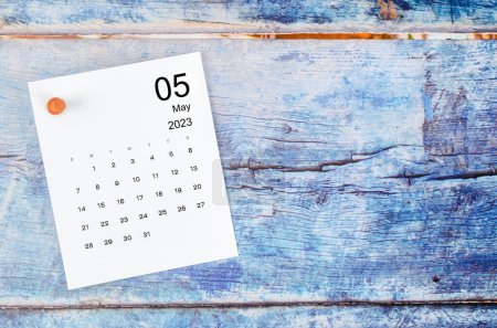 May 2023 monthly calendar and wooden push pin on blue wooden background.