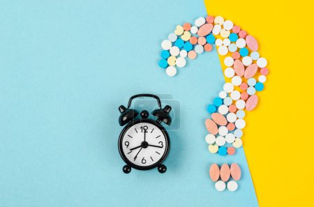 Photo for Question mark from laid out of medicine pills with Alarm Clock on blue background. - Royalty Free Image