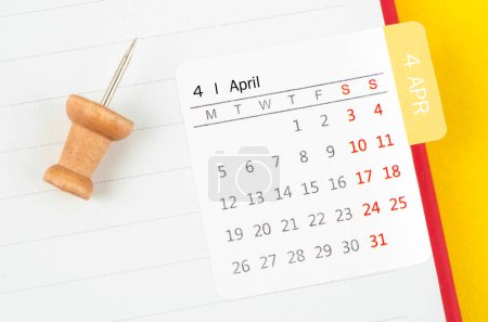 Photo for April mini calendar on a white note book with wooden push pin on yellow background. - Royalty Free Image