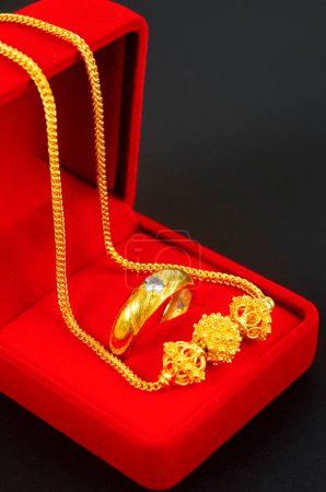 Foto de Collar de oro y colgante en forma de corazón y anillo de oro en caja de terciopelo rojo en negro. - Imagen libre de derechos
