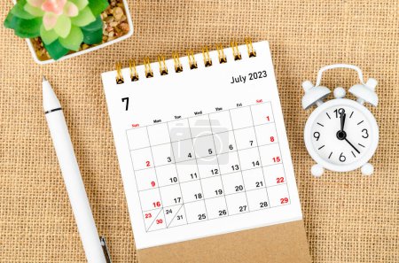 Foto de Julio 2023 Calendario mensual de escritorio para que el organizador planifique 2023 años con despertador y bolígrafo en el fondo del saco. - Imagen libre de derechos