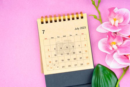 Juli 2023 Kalenderschreibtisch und rosa Orchidee auf rosa Hintergrund.