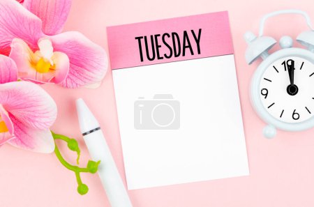 Blanko-Notizpapier für Dienstag und Orchidee mit Wecker auf rosa Hintergrund für Ihren Text oder Ihre Nachricht.