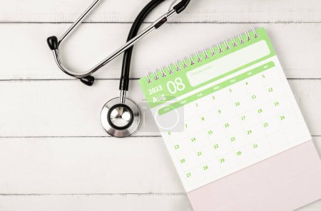 August 2023 Schreibtischkalender und Stethoskop Medical auf Holzgrund, Zeitplan zur Überprüfung gesunder Konzepte.