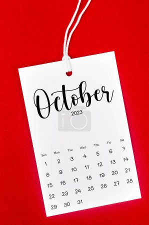 October 2023 calendar page for 2023 year hanged on white rope on Red background.