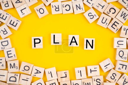 The PLAN word on wooden cubes. Alphabet blocks with heap of letters on yellow background.
