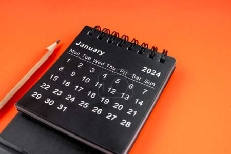 Foto de Enero 2024 calendario de escritorio con lápiz sobre fondo de color naranja. - Imagen libre de derechos