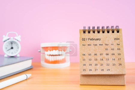Téléchargez les photos : Calendrier mensuel de février pour 2024 ans et modèles de prothèses dentaires sur la table avec réveil. Concepts de santé dentaire. - en image libre de droit