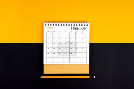 Téléchargez les photos : Vue du dessus du calendrier de bureau et du crayon de février 2024 sur couleur jaune et noire. - en image libre de droit