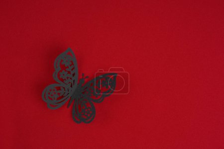 Foto de Una escultura de mariposa de papel negro sobre fondo de tela roja. Posición con espacio de copia. - Imagen libre de derechos