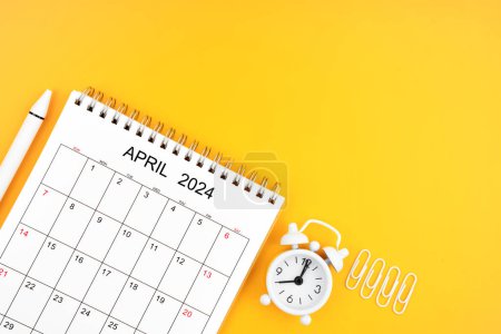 April 2024, Monthly desk calendar for 2024 year and alarm clock with paper clips on yellow color background. Position with copy space.