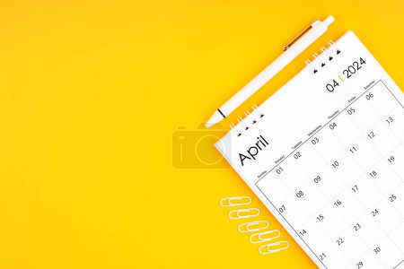 April 2024, Monthly desk calendar for 2024 year and pen with paper clips on yellow color background. Position with copy space.