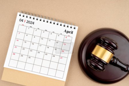 Schreibtischkalender für April 2024 und Richterhammer auf braunem Hintergrund.