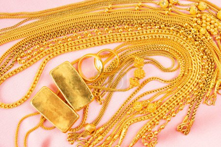 Many gold necklaces and gold bars on pink velvet cloth background.