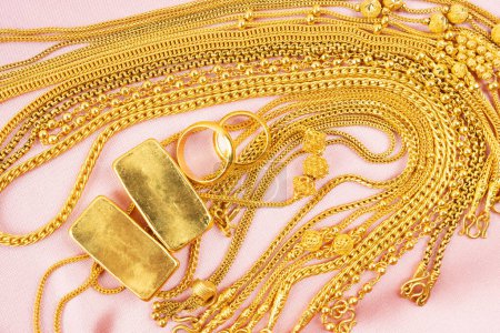 Many gold necklaces and gold bars on pink velvet cloth background.