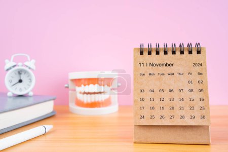 Noviembre calendario de escritorio mensual para 2024 año y dentaduras postizas modelo sobre la mesa con reloj despertador. Conceptos de salud dental.