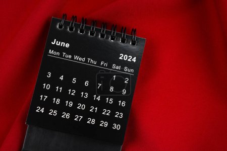 June 2024 Black spiral desktop calendar on red color textile.