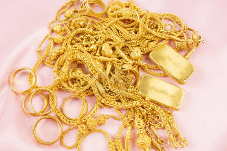 Many gold necklaces and gold bars on pink color cloth background.