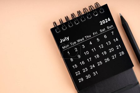Juli 2024 Schwarzer Spiralkalender und Holzstift auf gelbem Hintergrund.