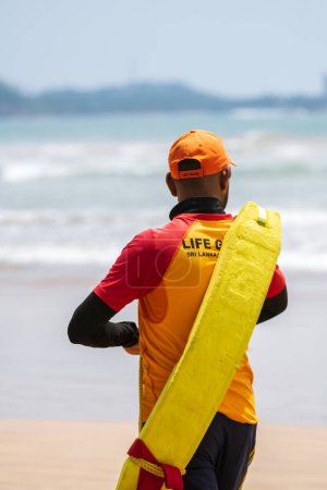 Foto de Lifeguard on duty, Walking on the sandy beach while carrying a rescue tube on the shoulder, lifeguard rear view photo. - Imagen libre de derechos