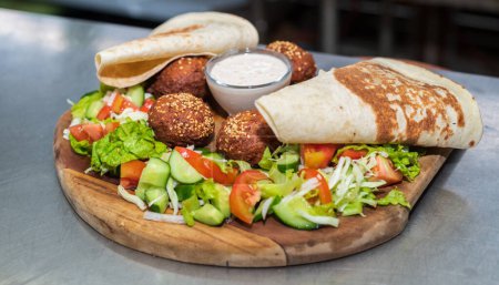 Foto de Delicious starter Falafel dish on a wooden plate in the Lebanese restaurant kitchen. flatbread, vegetable salad, and tahini sauce. - Imagen libre de derechos