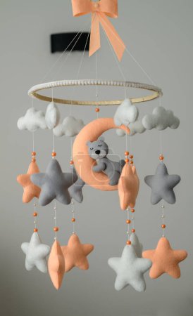 Baby crib mobile hanging in the nursery room, orange and grey pastel-colored theme, sleeping bear on the moon surrounded with stars.