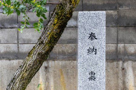 Photo for Tree and shrine marker stone, Jiohachiman Shrine, Kanazawa, Japan. TRANSLATION: donated (tree); natsume, or jujube tree. - Royalty Free Image