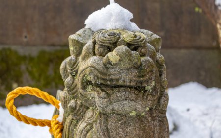 Komainu, oder Löwenhund, Statue im Winterschnee mit heiligem Shimenawa-Seil am kleinen lokalen Schrein, Kanazawa, Japan.